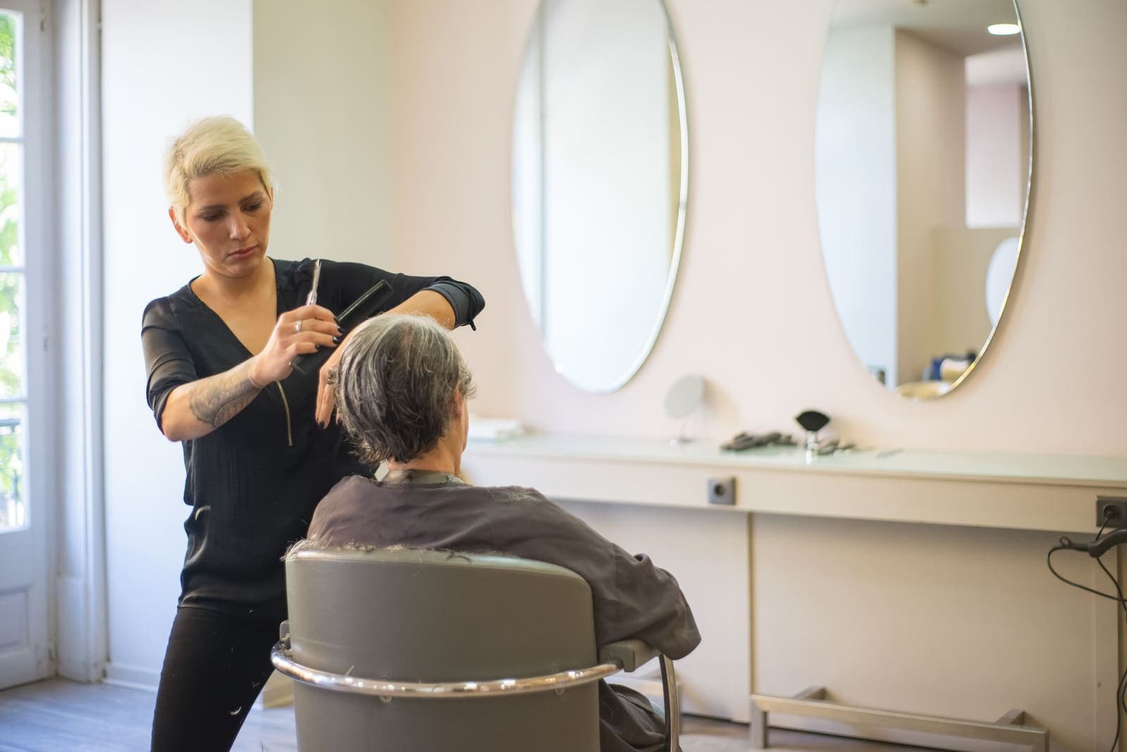 Cabeleireira a cortar o cabelo de uma cliente sénior num salão luminoso