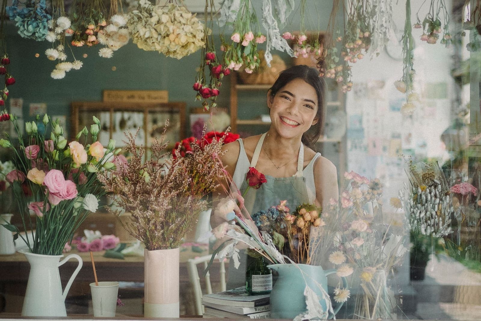 Florista sorridente entre flores na sua loja, vista através da montra