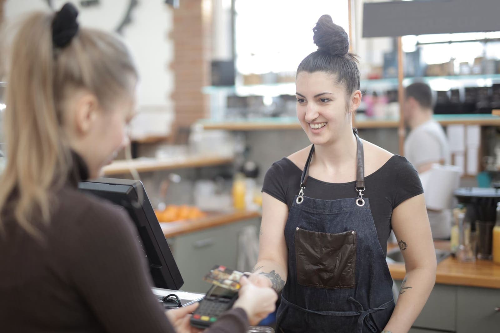 Barista sorridente a atender uma cliente ao balcão de um café